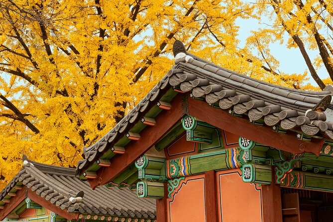Dancheong paintwork in green and vermilion under a palace eave, framed by yellow ginkgo